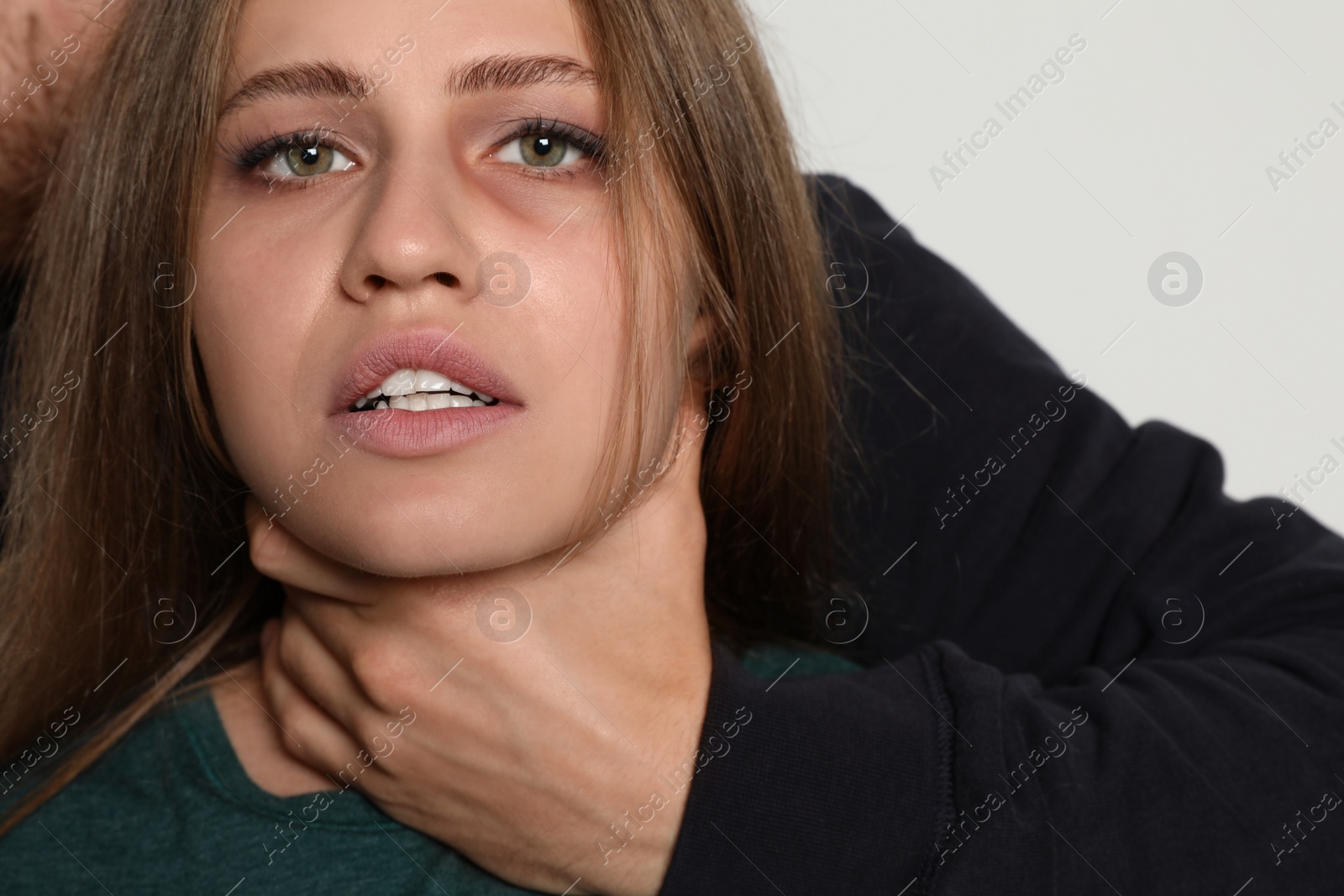 Photo of Man choking young woman on light background. Stop sexual assault