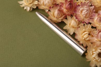 Photo of One metal bullet and beautiful flowers on green background, closeup. Space for text