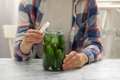 Photo of Woman pickling glass jar of cucumbers at white marble kitchen table, closeup