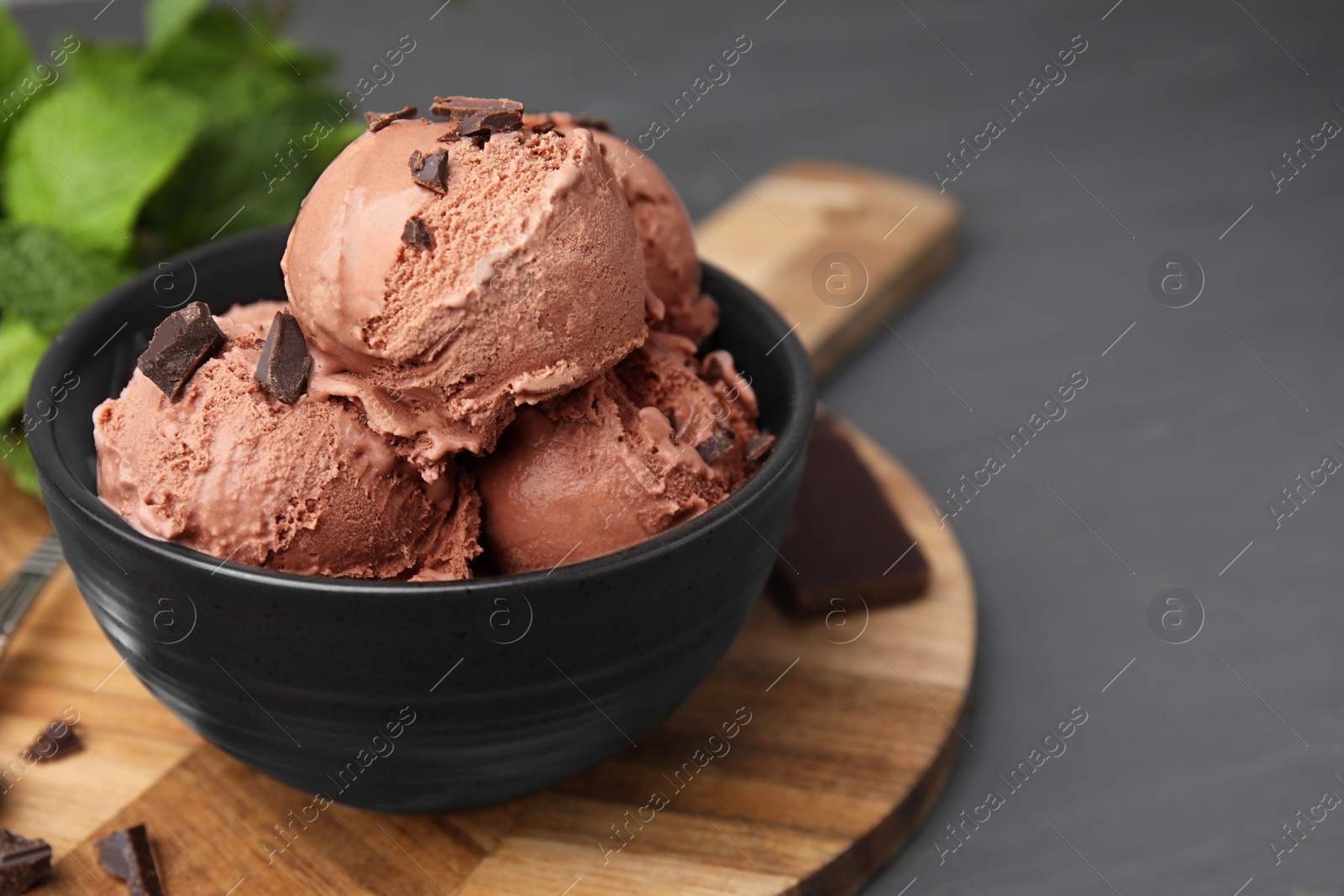 Photo of Bowl with tasty chocolate ice cream on grey wooden table, closeup. Space for text