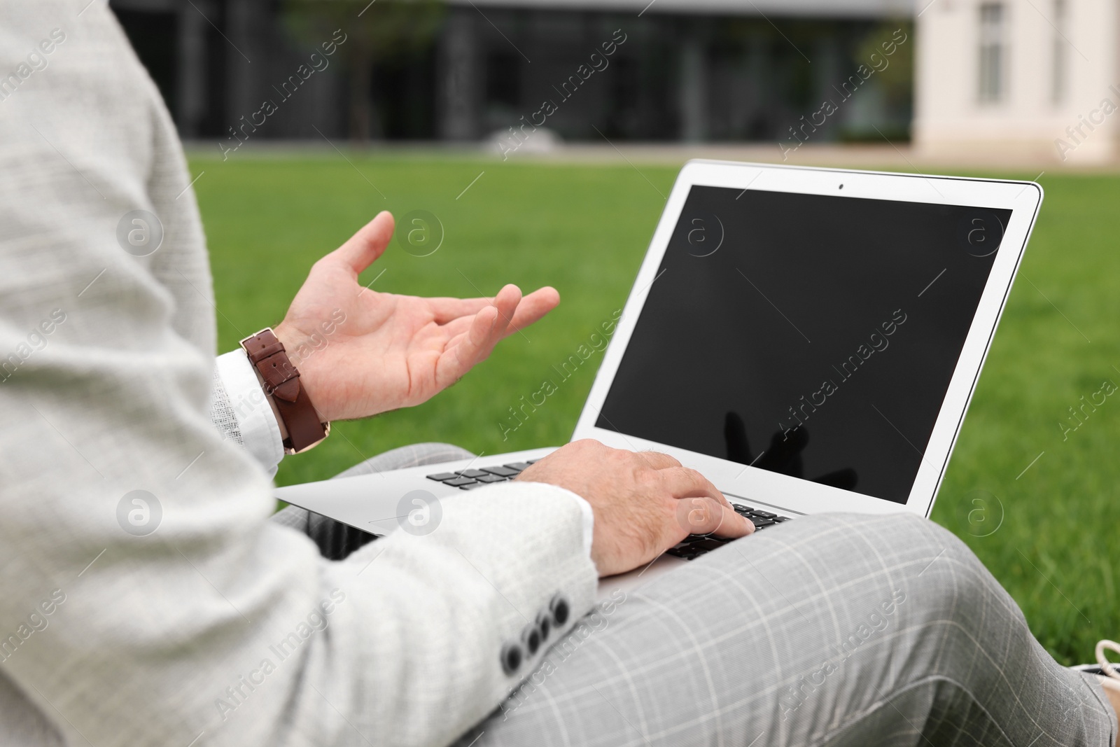 Photo of Businessman with laptop on green grass outdoors, closeup