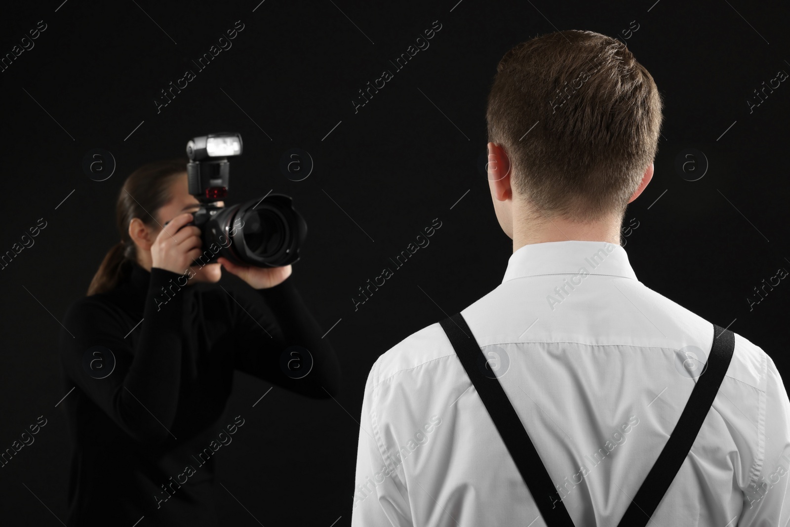 Photo of Professional photographer taking picture of man on black background, selective focus