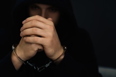 Man detained in handcuffs against dark background. Criminal law