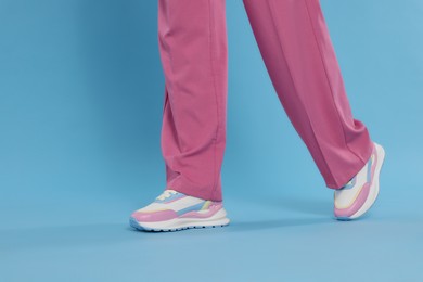 Woman wearing pair of new stylish sneakers on light blue background, closeup