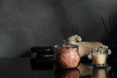 Photo of Glass jar with natural sea salt, beautiful flowers, candle and spa stones on mirror surface