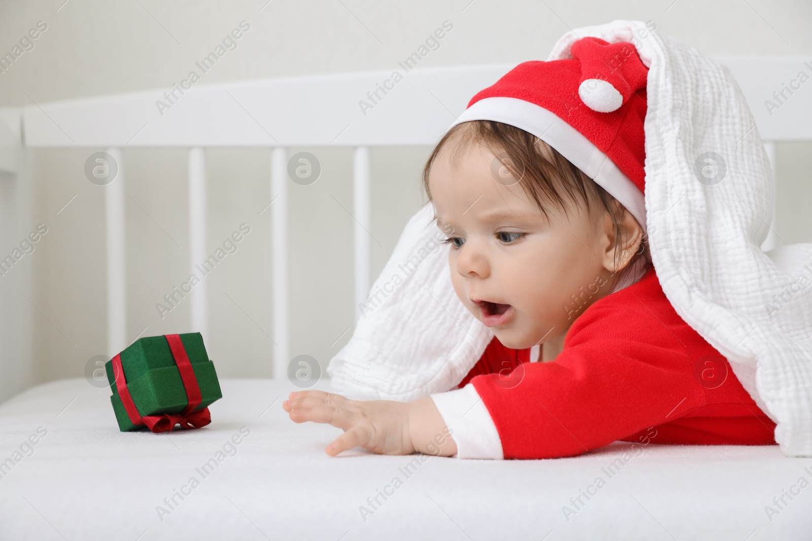 Photo of Cute baby wearing festive Christmas costume with gift box in crib