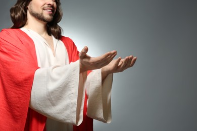 Photo of Jesus Christ reaching out his hands on grey background, closeup. Space for text