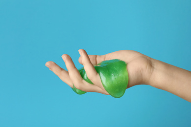 Photo of Woman playing with green slime on light blue background, closeup. Antistress toy