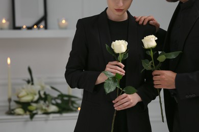 Couple with white roses mourning indoors, closeup and space for text. Funeral ceremony