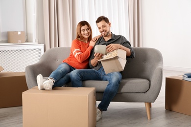 Photo of Couple unpacking cardboard box while resting on sofa in their new house. Moving day