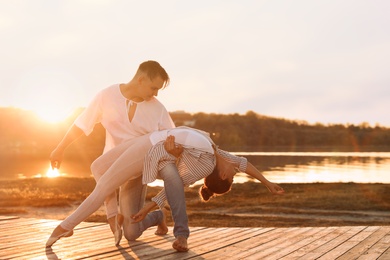 Beautiful young couple practicing dance moves near river at sunset