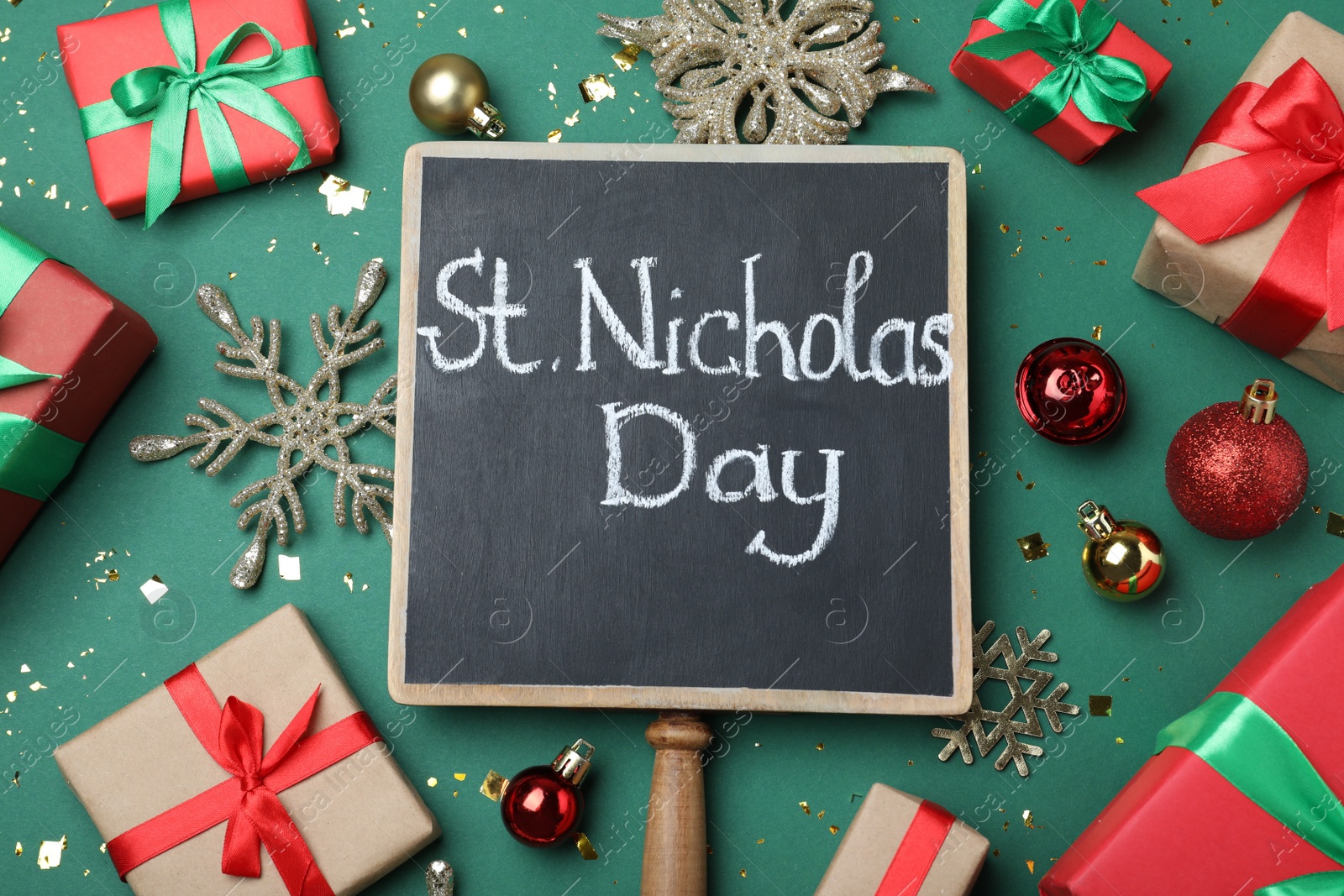 Photo of Small chalkboard with text St. Nicholas Day, gift boxes and festive decor on green background, flat lay
