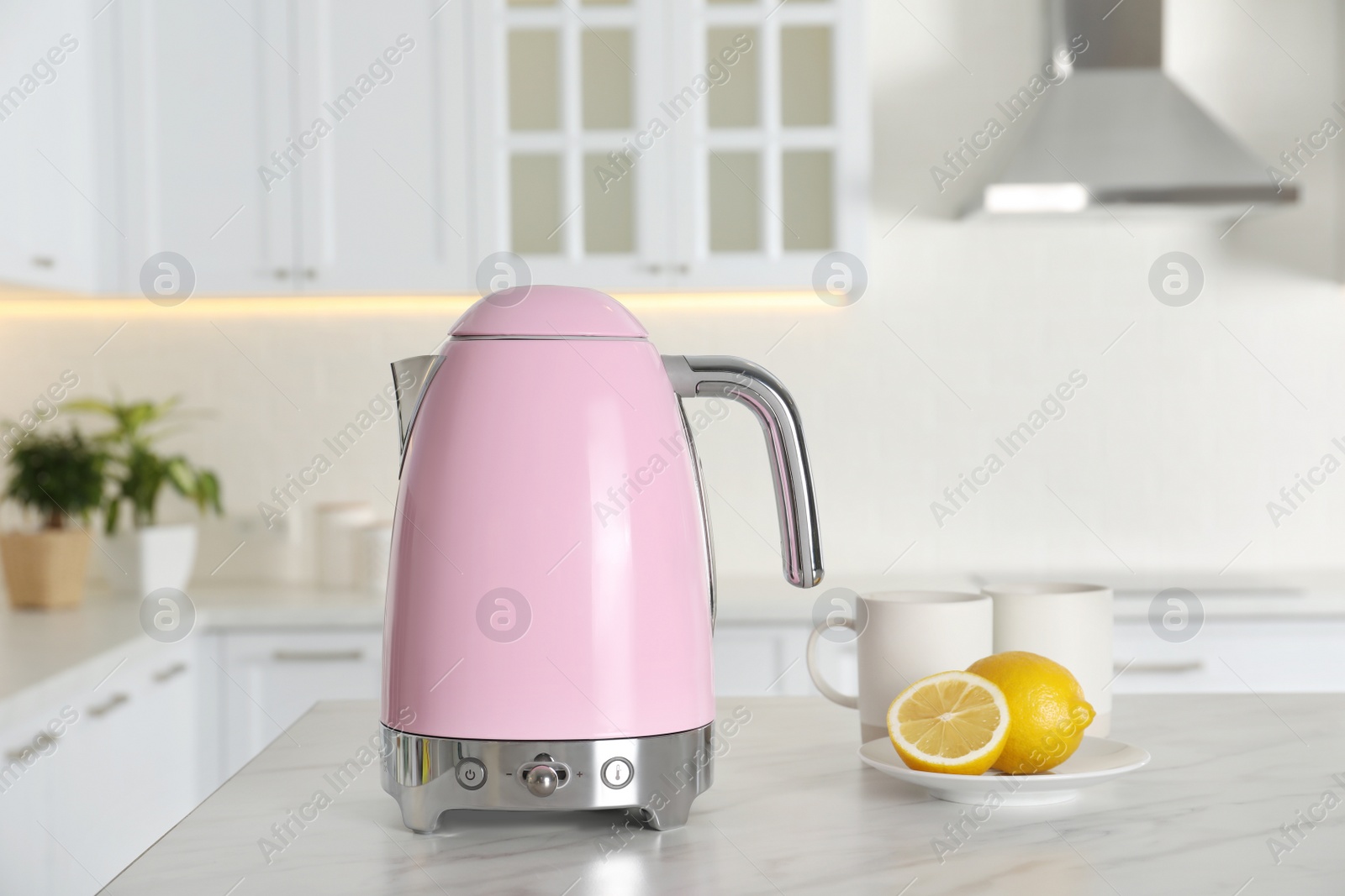 Photo of Modern electric kettle, cups and lemons on table in kitchen