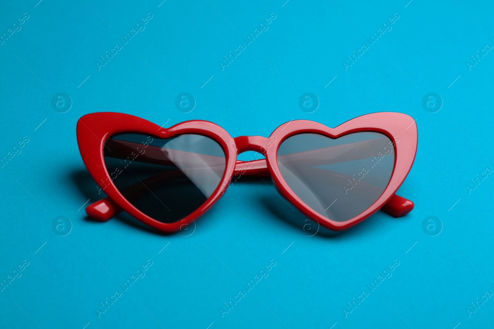 Photo of Stylish heart shaped sunglasses on blue background. Fashionable accessory