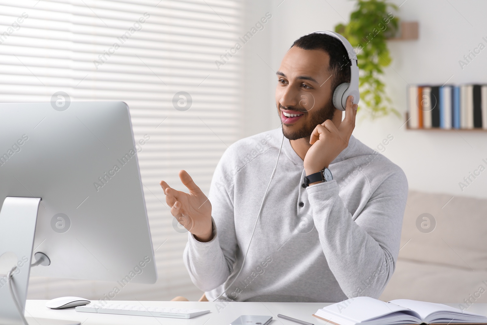 Photo of Young man with headphones working on computer at desk in room. Home office