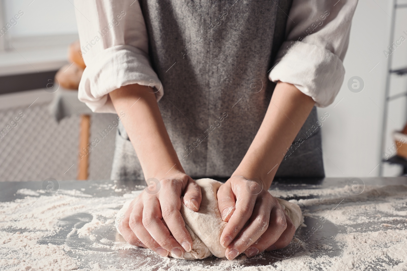 Photo of Woman kneading dough at table in kitchen, closeup