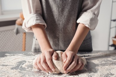 Photo of Woman kneading dough at table in kitchen, closeup