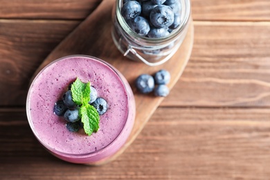 Glass of smoothie and jar with blueberries on wooden background, top view. Space for text