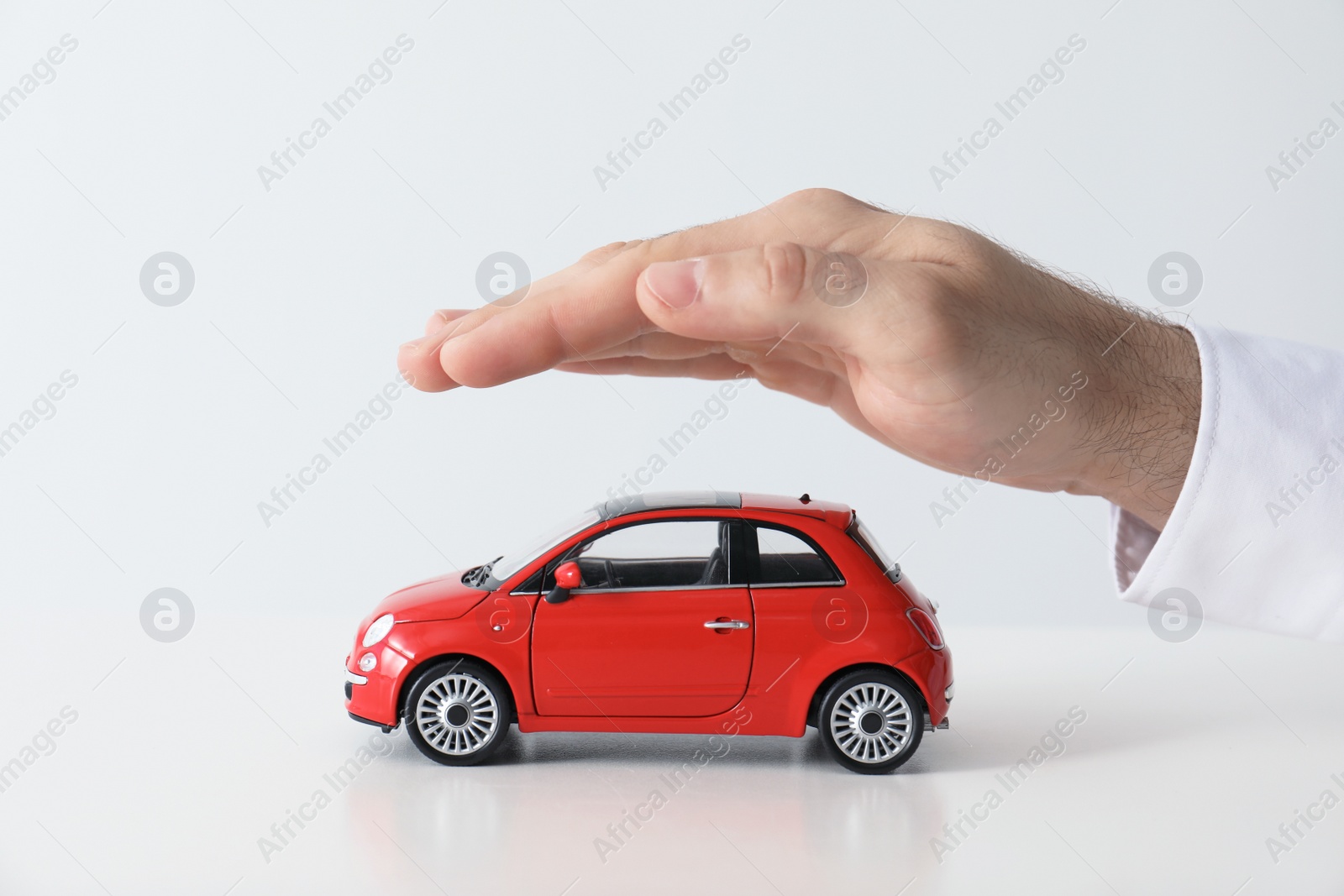 Photo of Male insurance agent covering toy car on white background, closeup