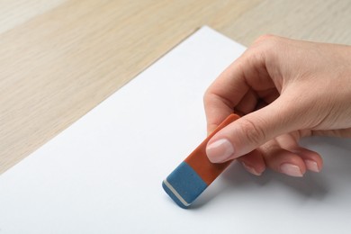 Photo of Woman erasing something in notebook at wooden table, closeup