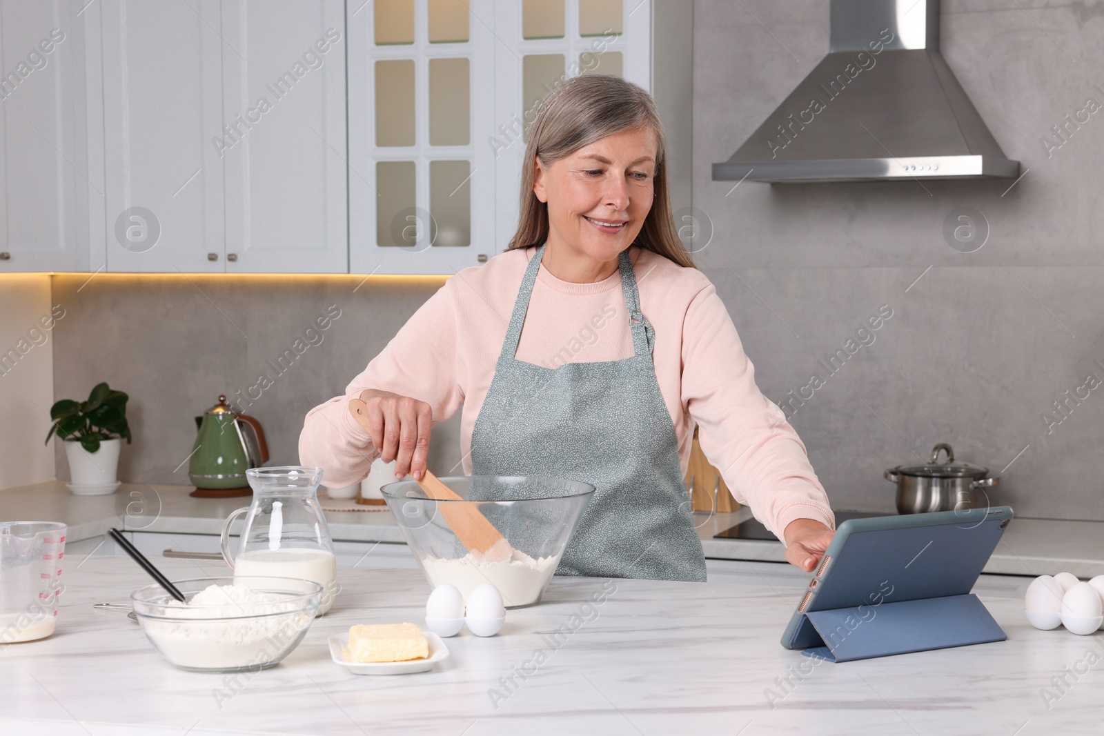 Photo of Senior woman reading recipe on tablet while cooking in kitchen. Online culinary book