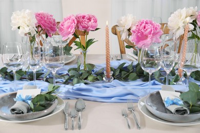 Photo of Beautiful table setting. Plates with greeting cards, napkins and branches near glasses, peonies, burning candles and cutlery on table indoors