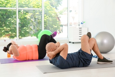 Overweight man and woman doing exercise on mats in gym