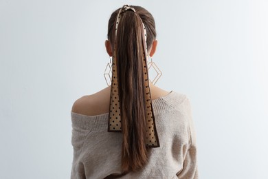 Young woman with stylish bandana on light background, back view