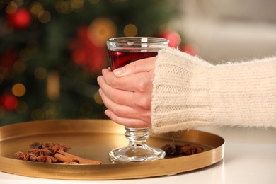 Photo of Woman holding glass cup of delicious mulled wine at white table against blurred background, closeup