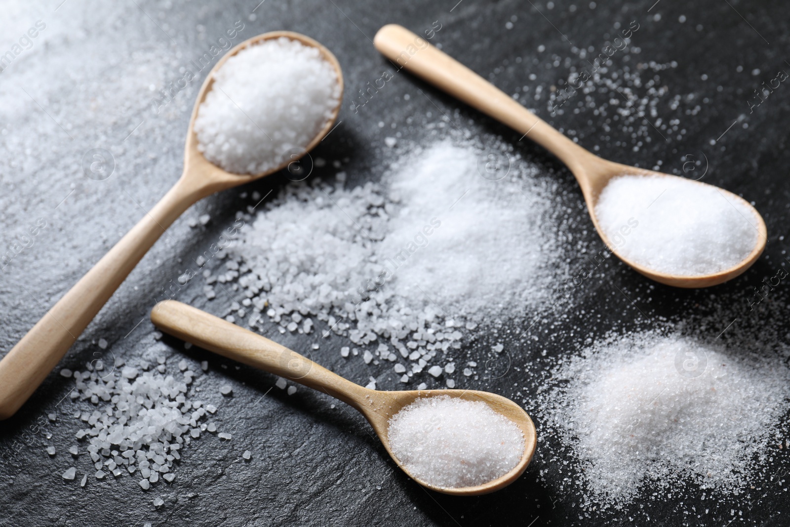 Photo of Organic salt in spoons on black table