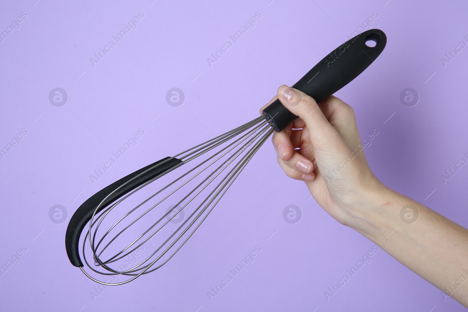 Photo of Woman holding metal whisk on lilac background, closeup