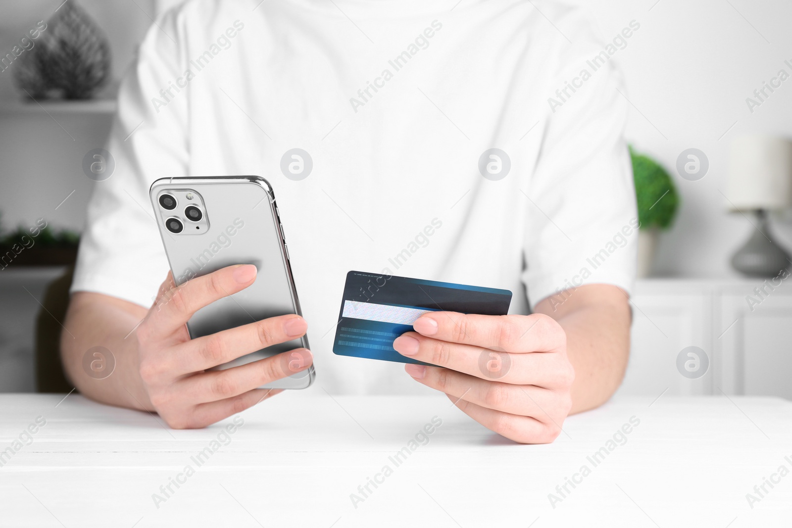 Photo of Online payment. Woman with smartphone and credit card at white table, closeup