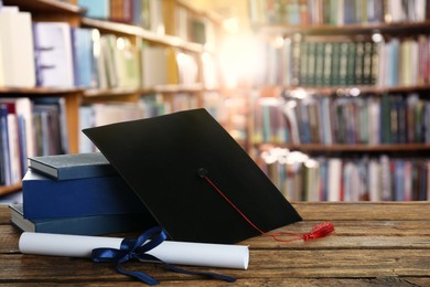 Image of Graduation hat, books and diploma on wooden table in library