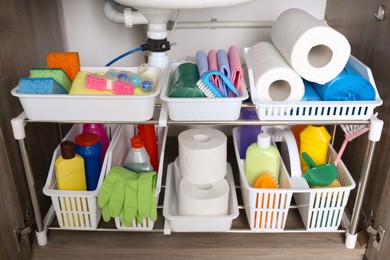 Photo of Open under sink cabinet with different cleaning supplies in kitchen