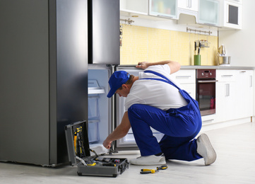 Photo of Male technician repairing broken refrigerator in kitchen