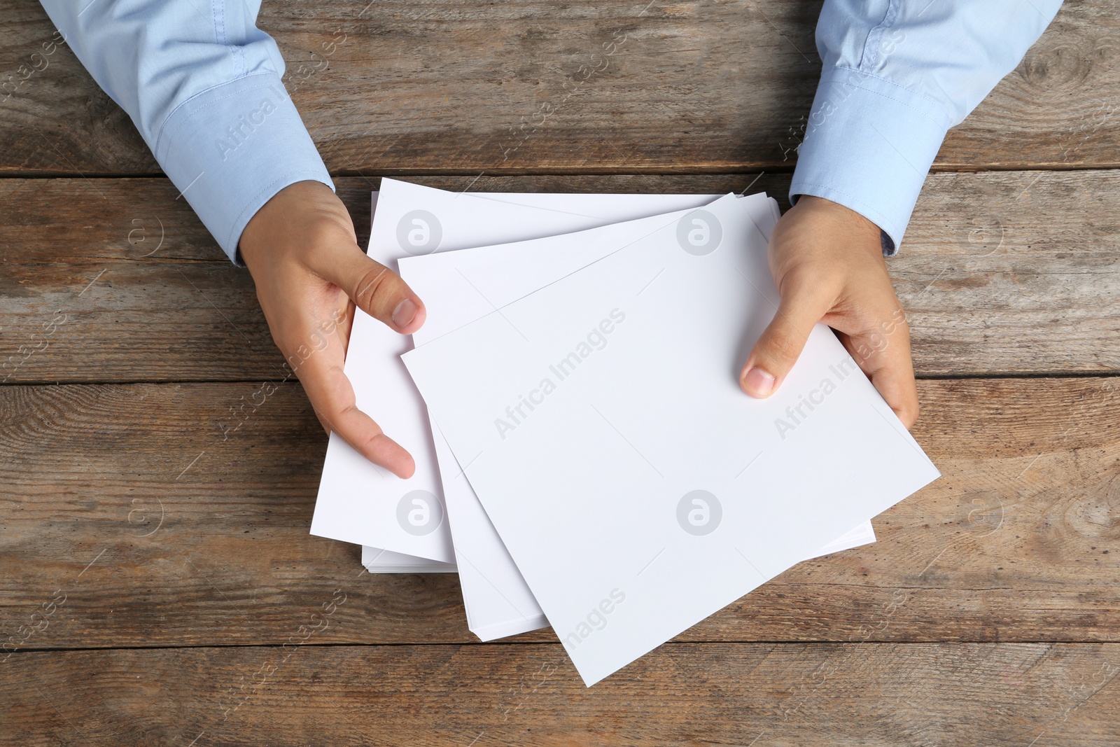 Photo of Man holding blank paper sheets for brochure at wooden table, top view. Mock up