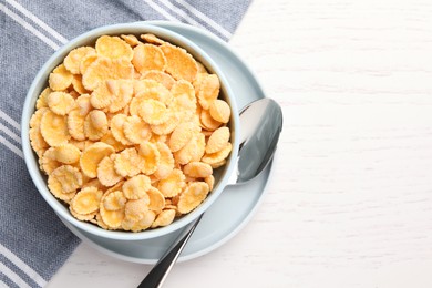 Photo of Bowl of tasty corn flakes and spoon on white wooden table, top view. Space for text