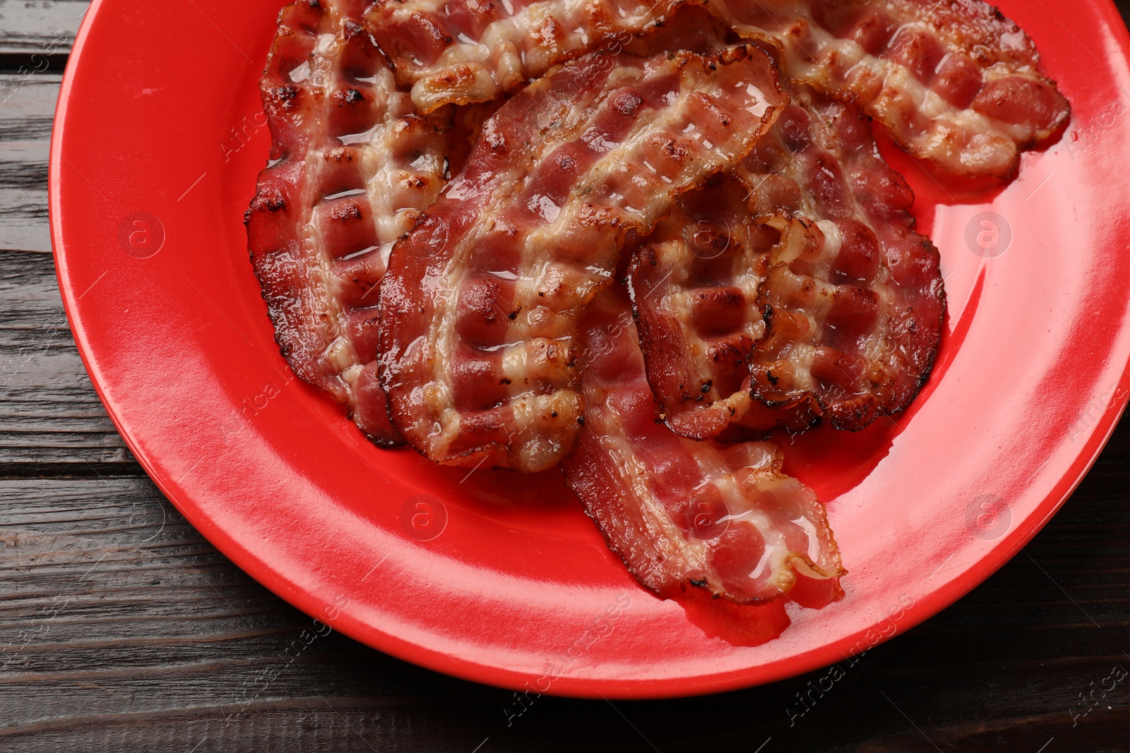 Photo of Plate with fried bacon slices on wooden table, top view