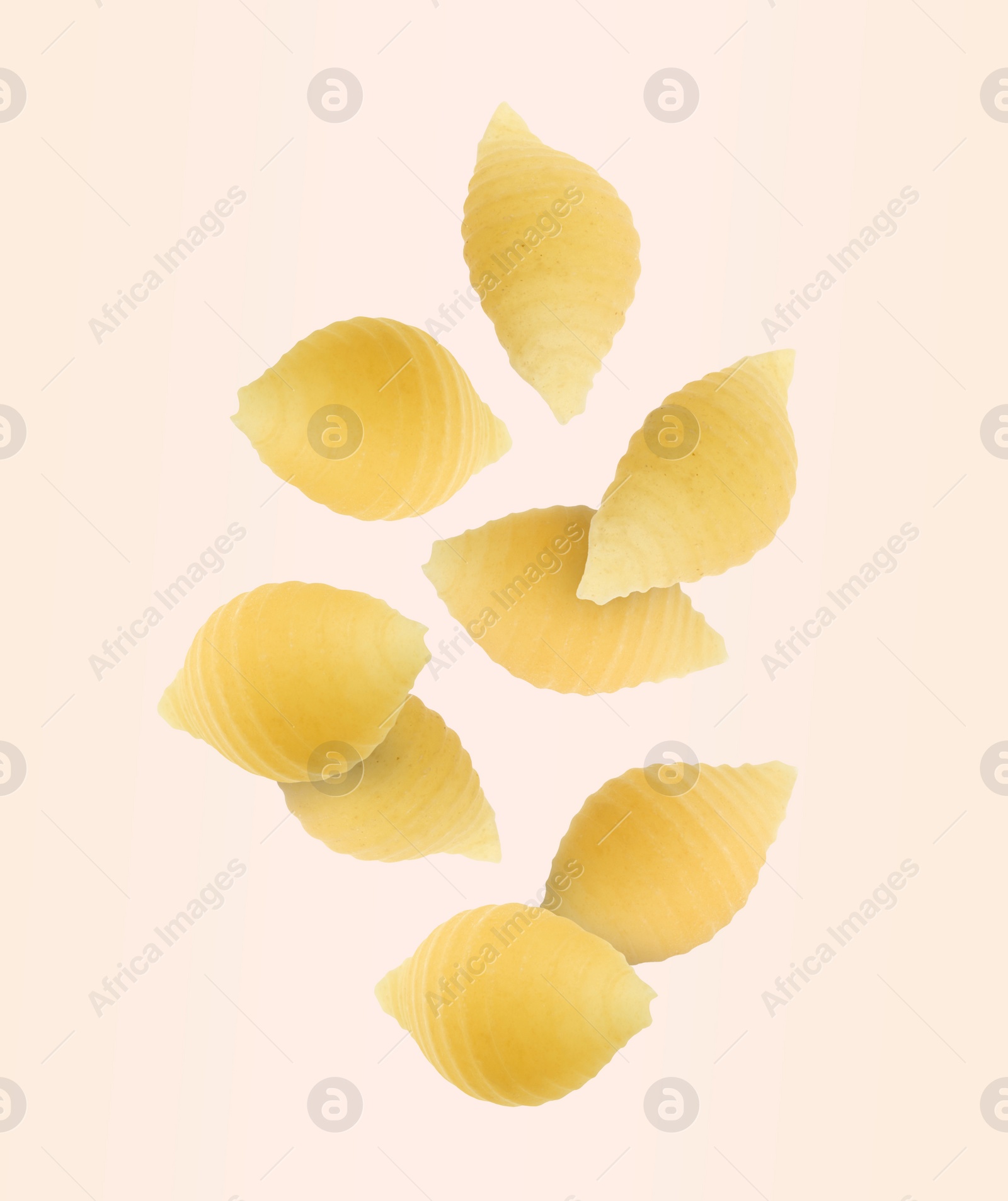 Image of Raw conchiglie pasta flying on beige background