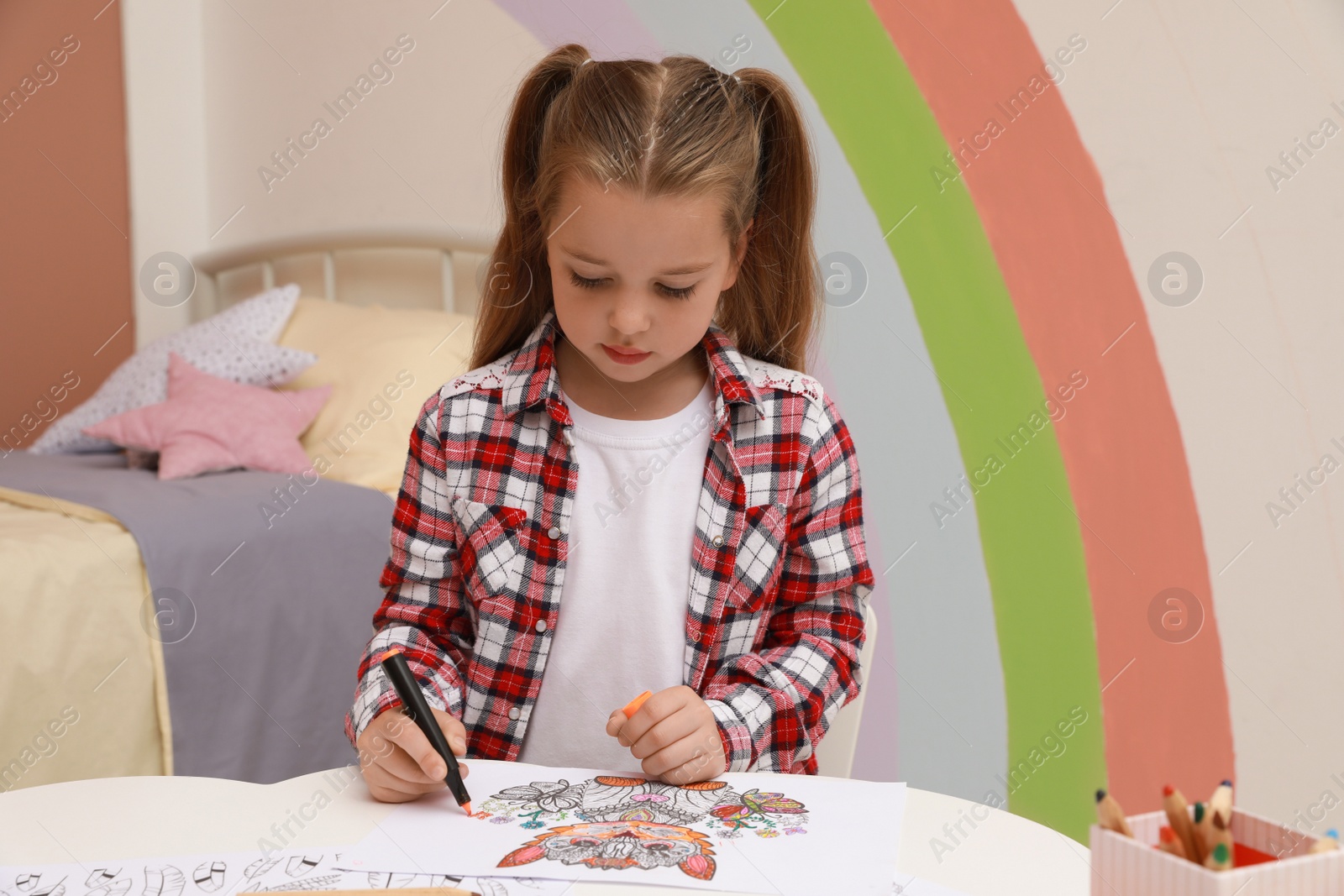 Photo of Little girl coloring antistress page at table indoors