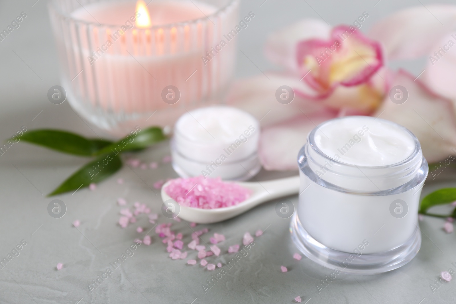 Photo of Beautiful spa composition with cosmetic products, flowers and candle on light grey table. Space for text