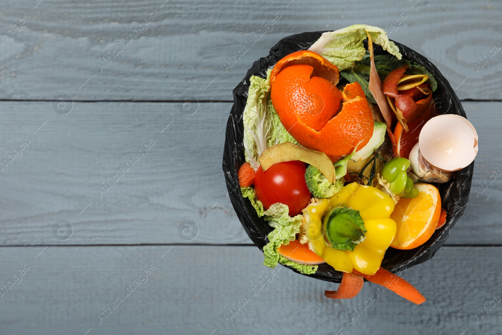 Photo of Natural garbage in trash bin on grey wooden background, top view with space for text. Composting of organic waste