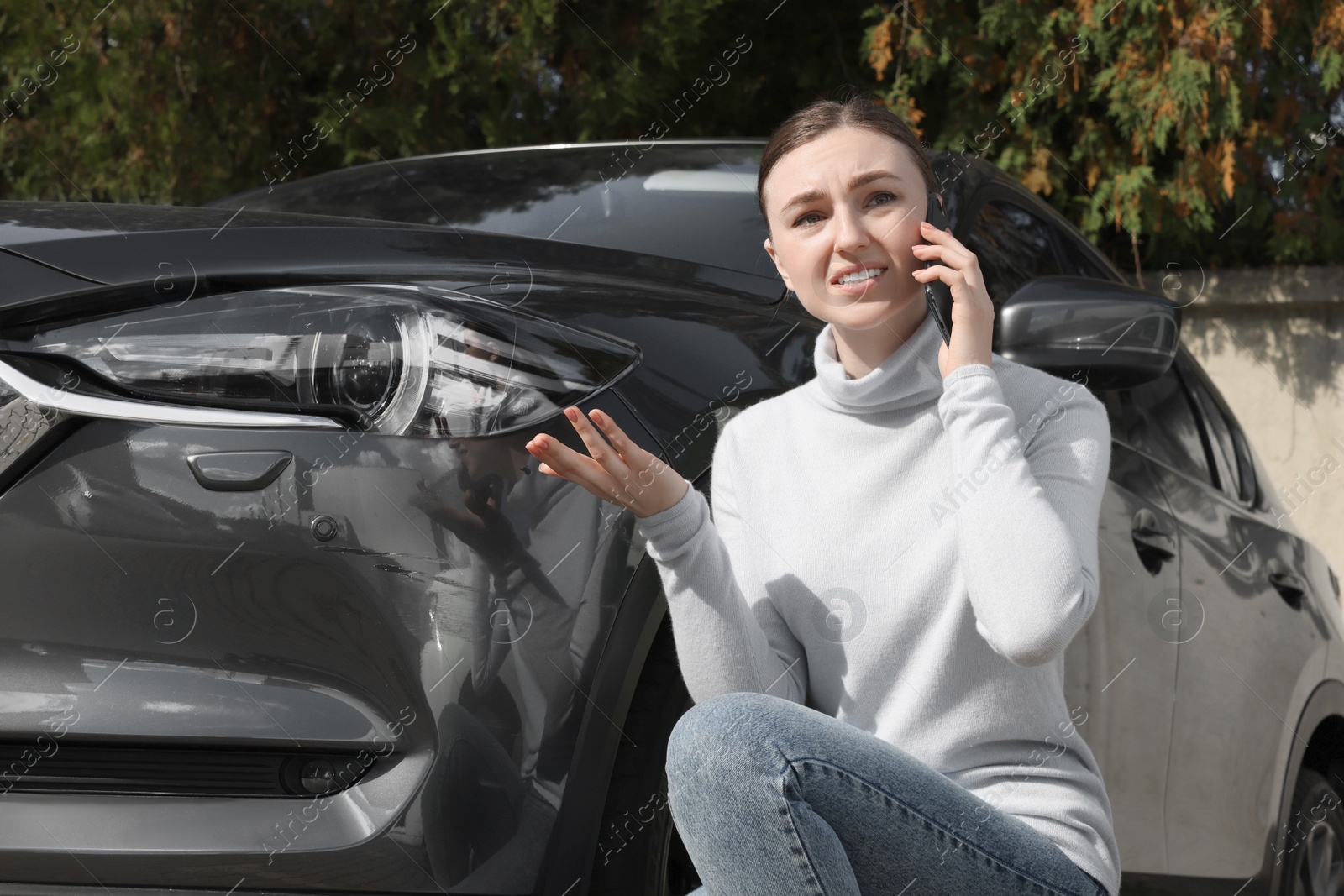 Photo of Stressed woman talking on phone near car with scratch outdoors