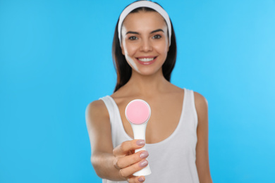 Photo of Young woman holding facial cleansing brush on light blue background. Washing accessory