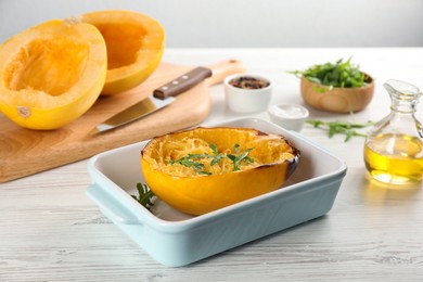 Photo of Half of cooked spaghetti squash with arugula in baking dish on white wooden table