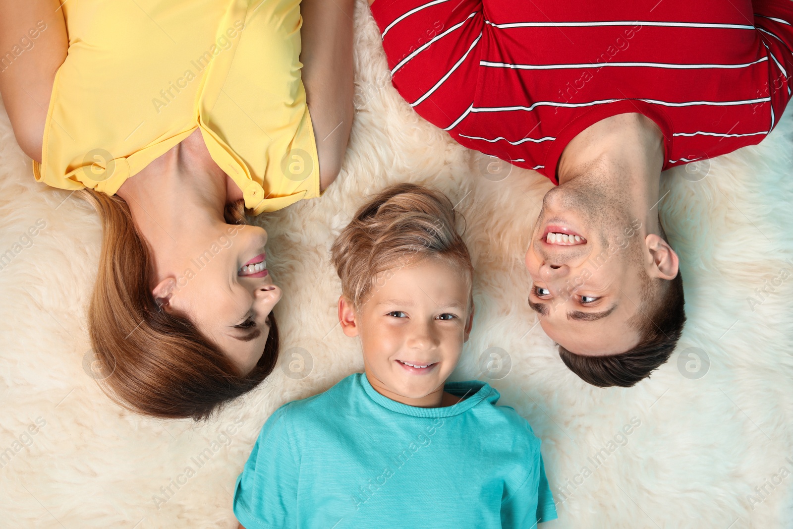 Photo of Little boy with mother and father lying on fuzzy rug, top view