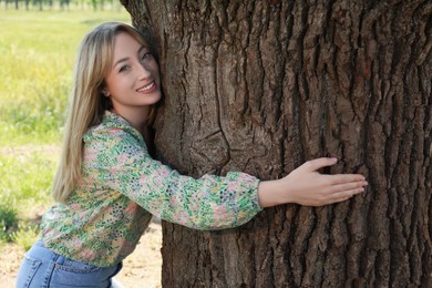 Beautiful young woman hugging tree trunk in forest