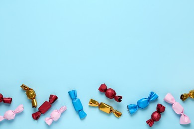 Photo of Candies in colorful wrappers on light blue background, flat lay