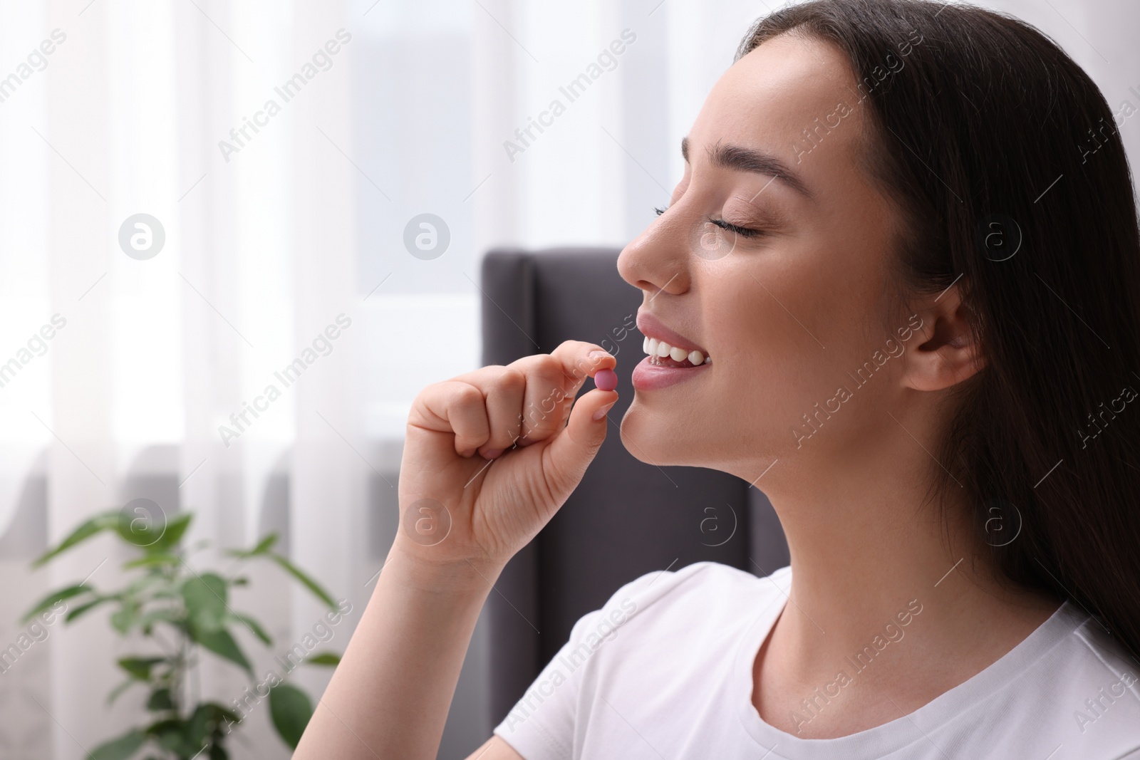 Photo of Beautiful young woman taking pill at home, space for text