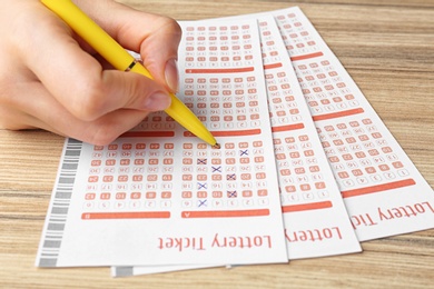 Woman filling out lottery tickets with pen on wooden table, closeup. Space for text